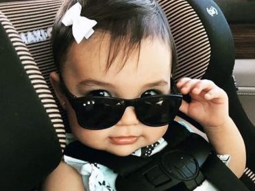 Cute baby with brown hair and sunglasses in a car seat