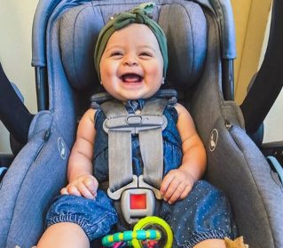 Cute baby in a blue outfit smiling in a car seat